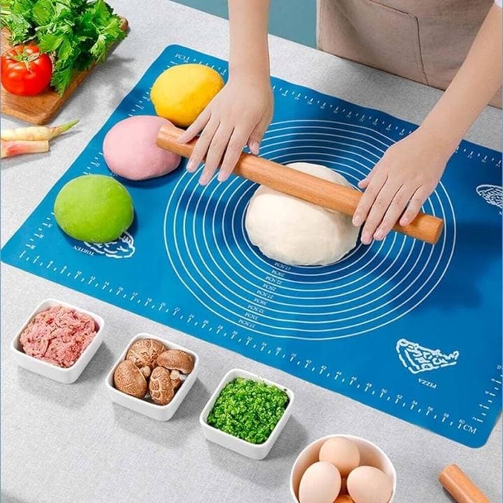 Person rolling dough on a blue baking mat with various ingredients around