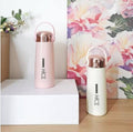 Two pink and white thermos bottles with 'NICE' branding on a wooden surface with a floral background.