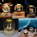 A 2x3 collage showing four views of a glowing decorative crystal ball night light on a wooden base. The top row shows the clear sphere with internal moon and couple illustrations under warm light; the bottom row shows the same light in a darker room with a planet scene and small astronaut figure.