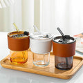 Three glass tumblers with leather sleeves and straws on a wooden tray.