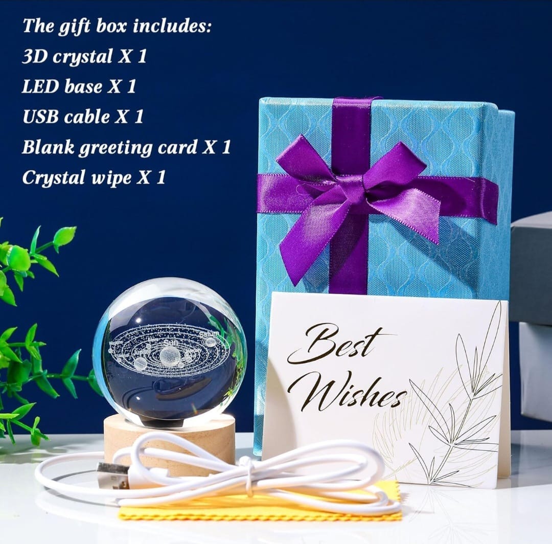 Gift set containing a 3D crystal ball with an LED base, a blue patterned gift box with a purple ribbon, a white greeting card that says 'Best Wishes', a USB cable, and a crystal wipe, displayed on a white surface against a dark blue background with product details listed in the top left.